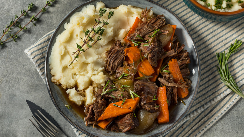 A plate of beef pot roast with fresh thyme and mashed potatoes.