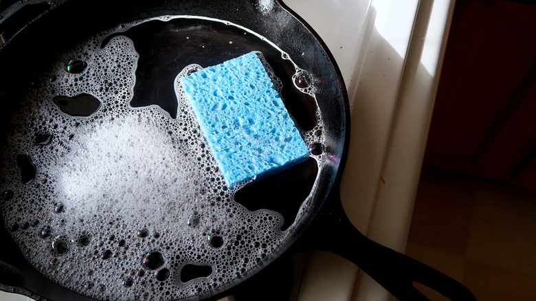 A person cleaning their cast iron pan with a sponge.