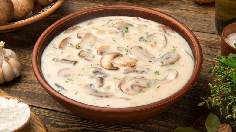 Cream of mushroom soup in a bowl alongside whole mushrooms and aromatics
