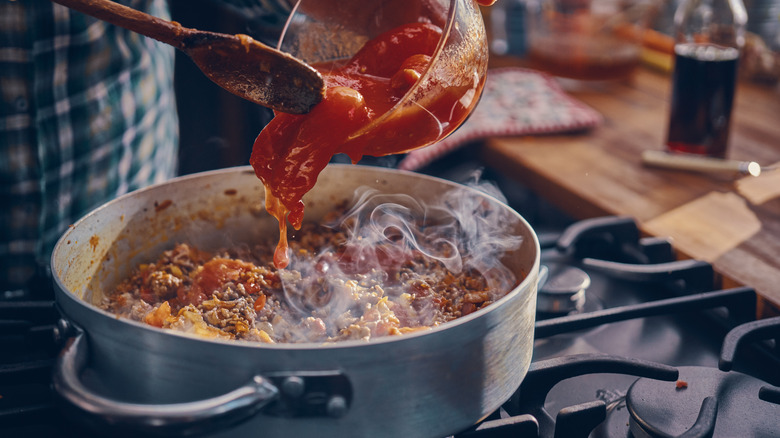 Pouring tomatoes into pasta sauce