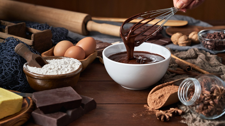 whisk pulled out of bowl of melted chocolate with baking ingredients