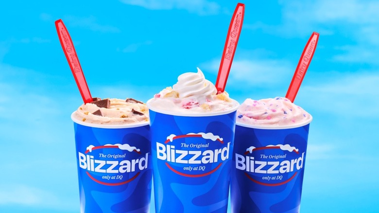 Three DQ Blizzards with red, long-handled spoons against a blue sky background