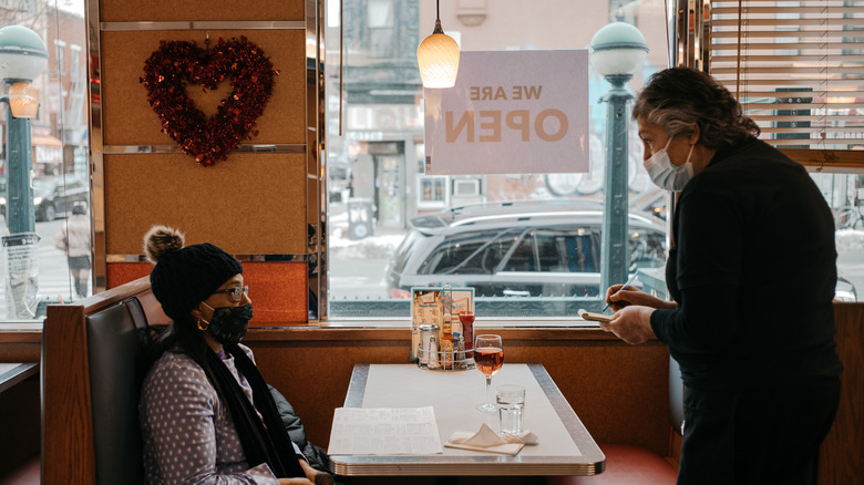 Waiter taking order from woman in diner booth