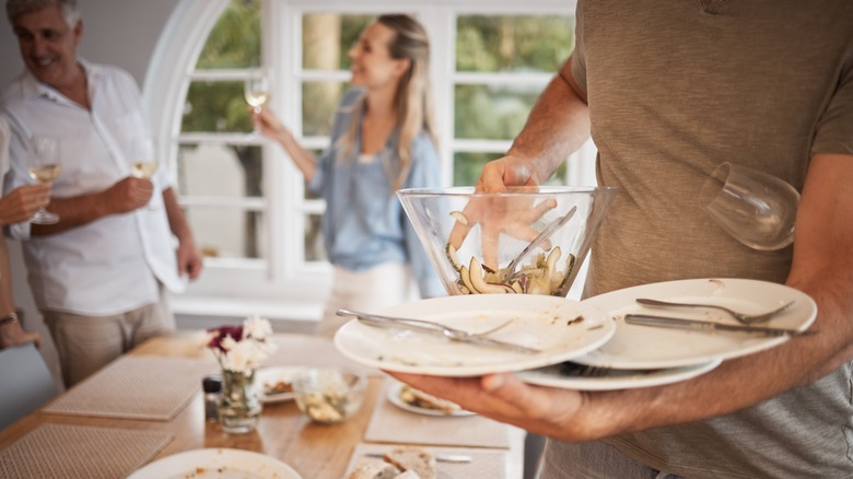 Host cleaning plates at dinner party