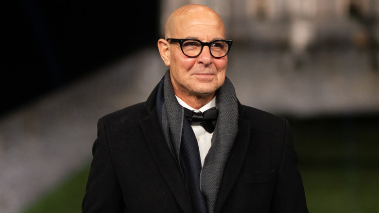 Stanley Tucci smiles at an event while wearing a full tuxedo and scarf