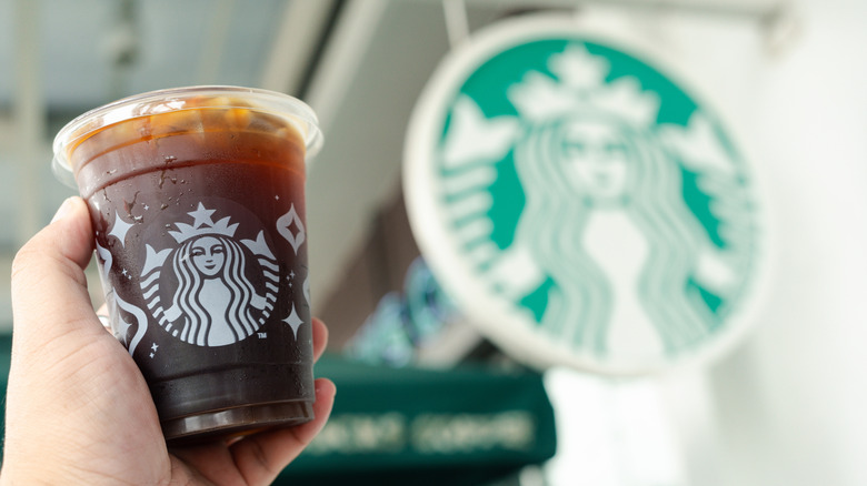 Starbucks iced coffee held in the air next to a Starbucks sign