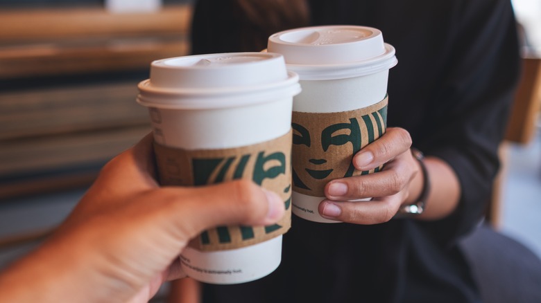 Two people toasting with Starbucks cups