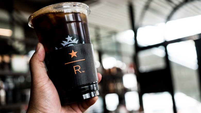 Hand holding a special Starbucks Reserve coffee cup in front of a Starbucks Reserve location