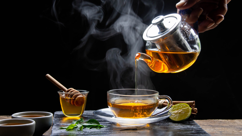 Pouring hot tea into clear cup on black slate