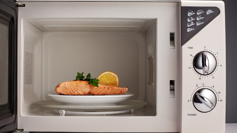 A plate of salmon garnished with lemon and parsley sits in an open microwave