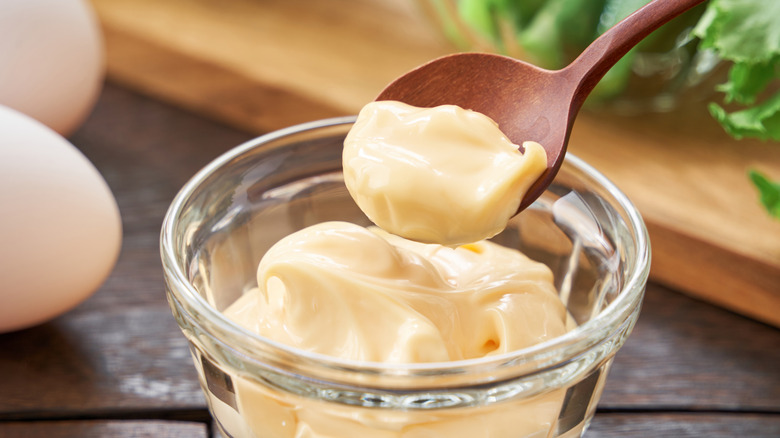 Someone scoops up a bit of mayo from a bowl with a wooden spoon.