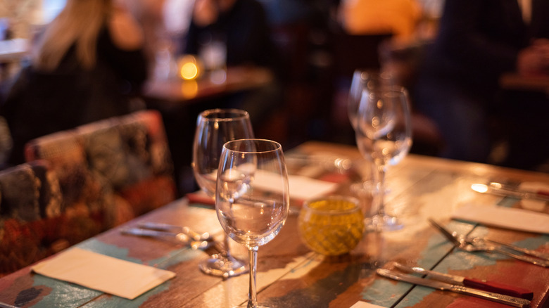 A restaurant table is set with wine glasses, napkins, and silverware