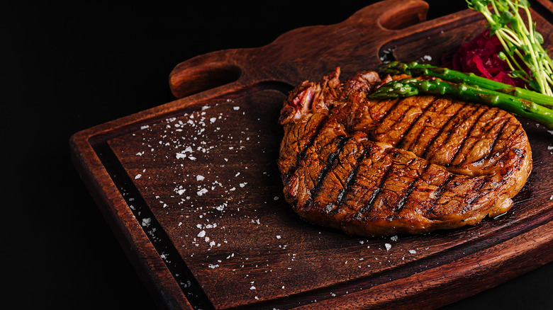 A grilled steak with asparagus rests on a wooden serving board