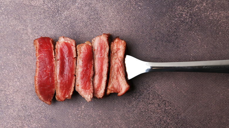 A fork holds slices of beef showing varying degrees of doneness against a gray background