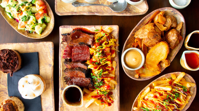 A variety of dishes including a salad, fries, potato skins, and more sit on a wooden table