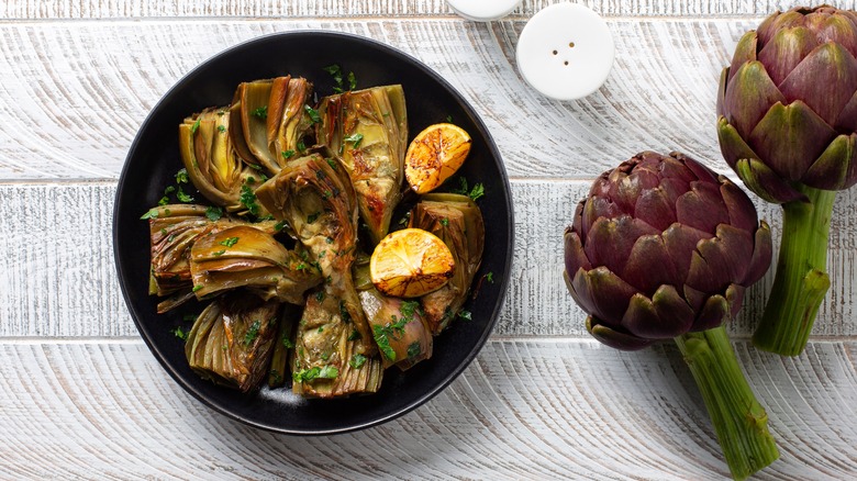 Artichokes with stems and bowl of cooked artichokes