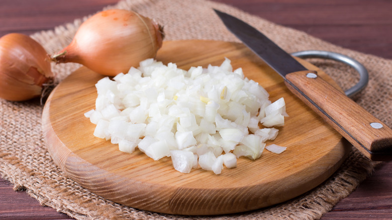 Chopped onions on round wood cutting board with knife