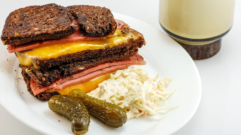 Fried bologna sandwich with yellow cheese, coleslaw, and pickles on a white plate