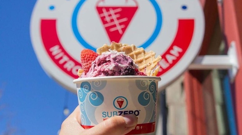 Hand holding berry ice cream cup in front of sign