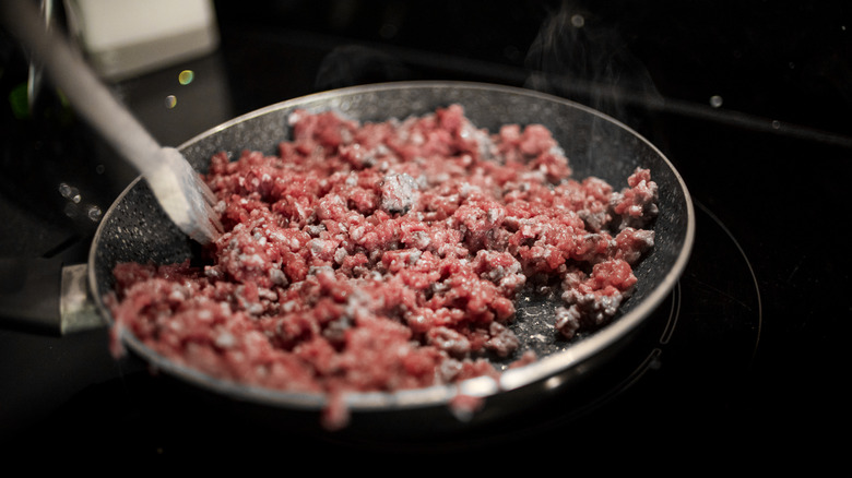 Ground beef is cooking in a pan, as someone uses a utensil to chop and toss it