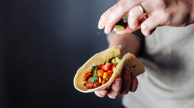 A person squeezing a lime on to a taco.
