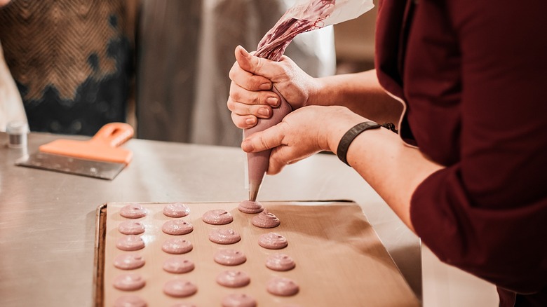 a person piping macaron shells on a baking sheet