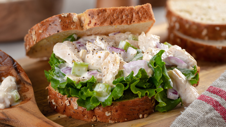 Open faced chicken salad sandwich with lettuce on wooden cutting board.