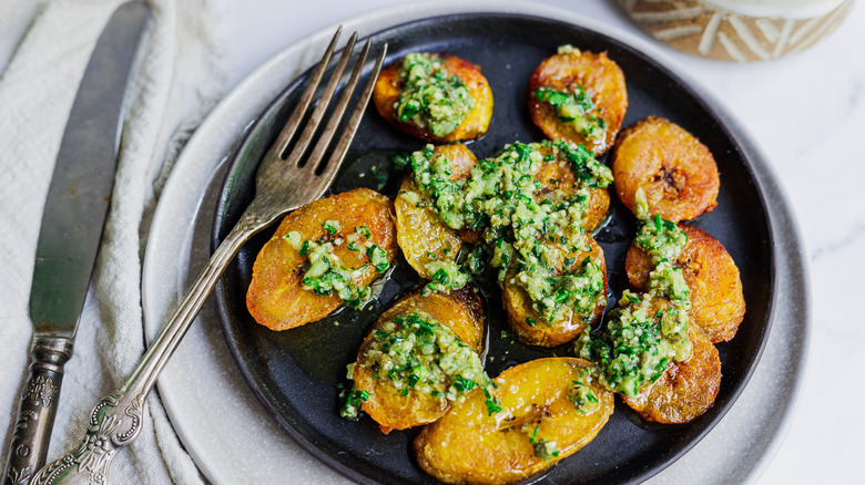 fried plantains with green sauce on black plate with fork and knife