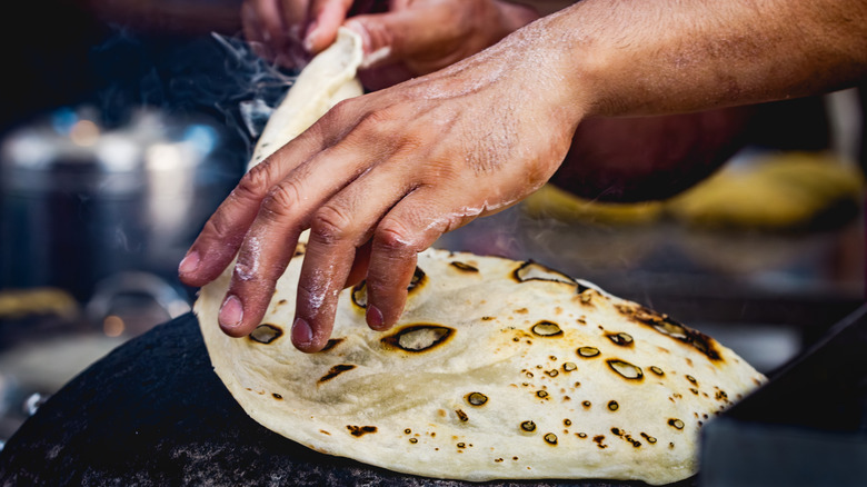 Hands turn over a tortilla in a frying pan