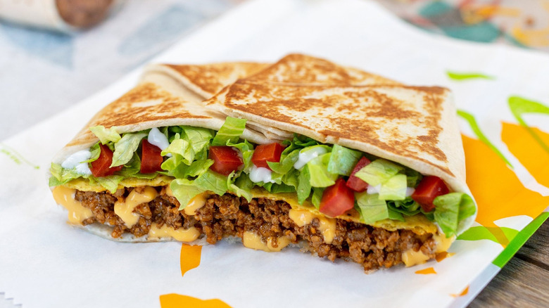 A Taco Bell Crunchwrap Supreme cut in half sits on its restaurant food wrapper