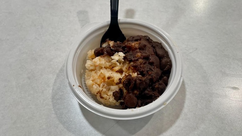 A small white dish of Taco Bell's Black Beans and Rice with a fork on a white table top