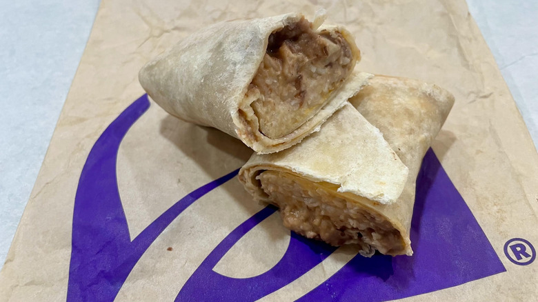 Two halves of a Taco Bell Cheesy Bean and Rice Burrito on a white table top
