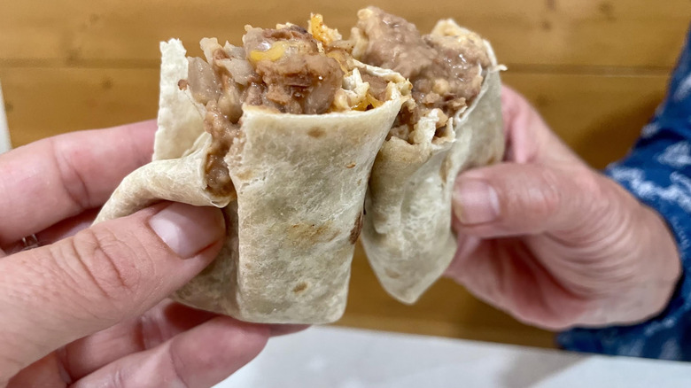 Two hands holding two halves of a Taco Bell Bean Burrito