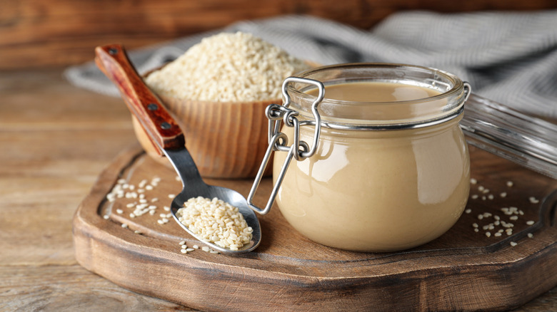 small jar of tahini with sesame seeds in background