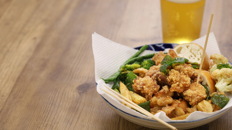 bowl of Taiwanese popcorn chicken with fried basil, vegetable, and a glass beer