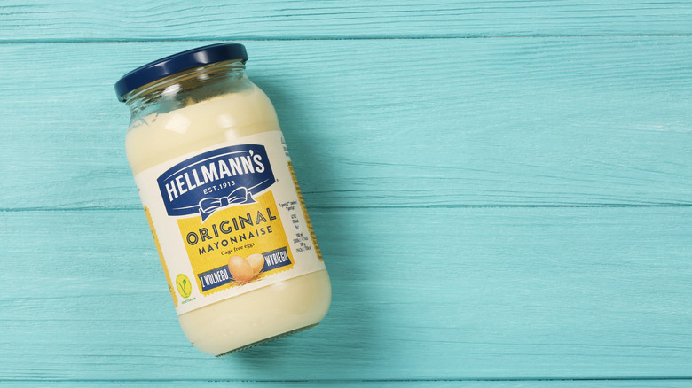 A jar of mayonnaise rests on its side on a blue wooden surface