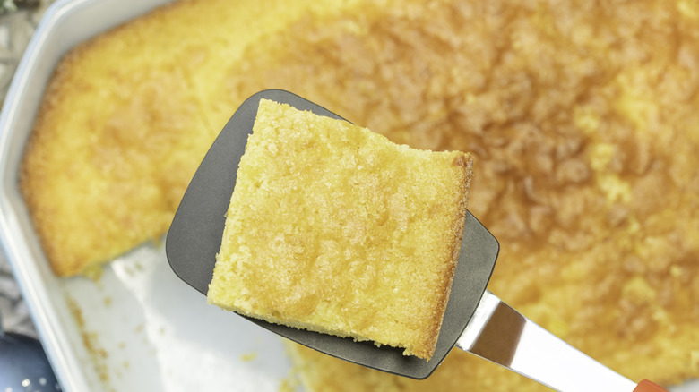 Close up slice of baked cornbread on a spatula in white casserole dish