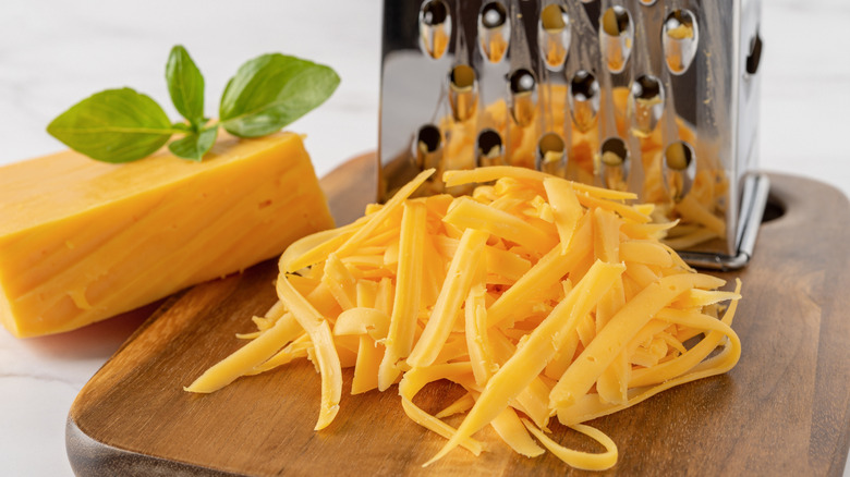 Block of shredded cheese with shredded portion next to boxed grater