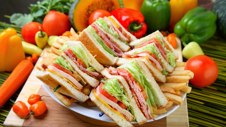 Club sandwich on a plate with fries and vegetables in the background
