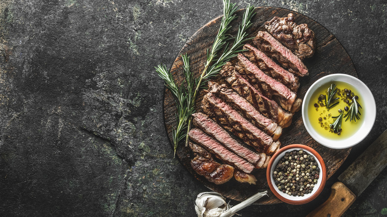 Sliced, cooked steak next to herb infused olive oil and pepper