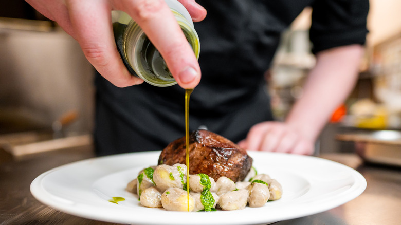 Drizzling olive oil over seared meat and gnocchi