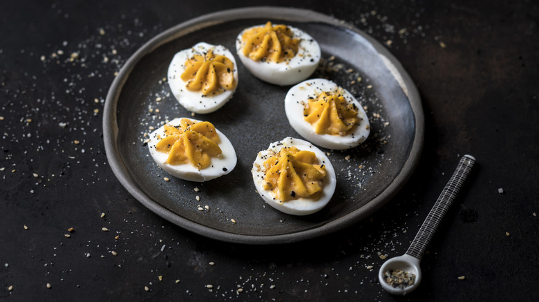 black plate with deviled eggs topped with coarse pepper
