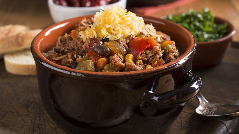 Bowl of chili topped with cheese with a dish of green onions in the background
