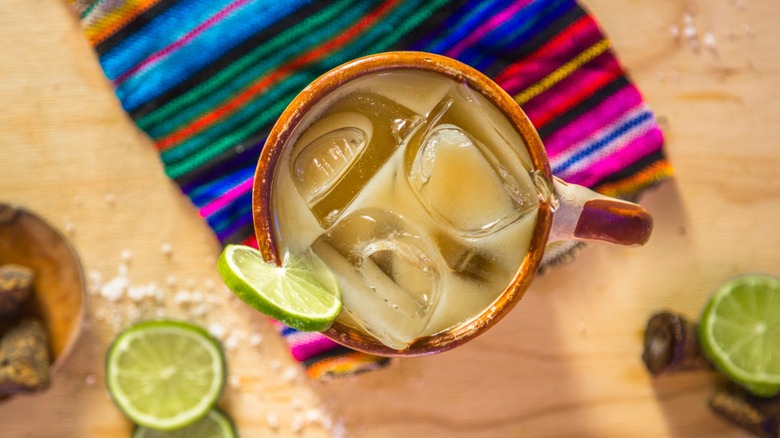 Top view of tejuino in a glass garnished with lime, surrounded by limes and Mexican brown sugar and salt