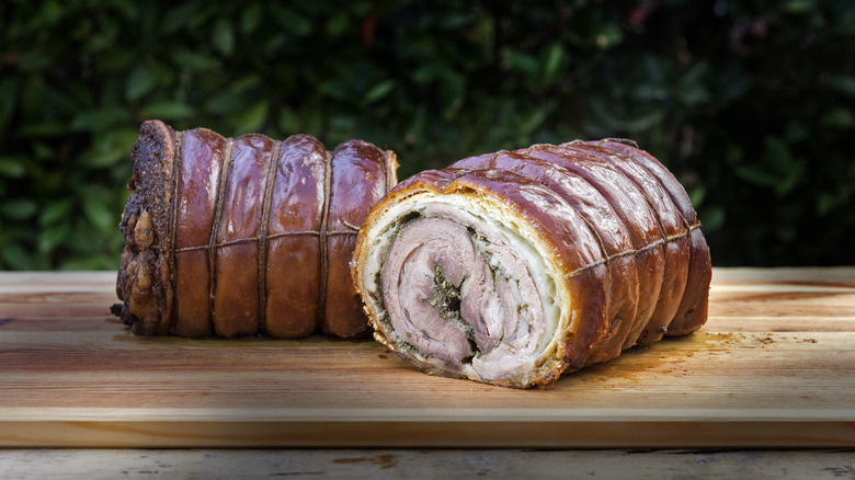 A gorgeously roasted porchetta sits, still trussed, on a wooden carving board