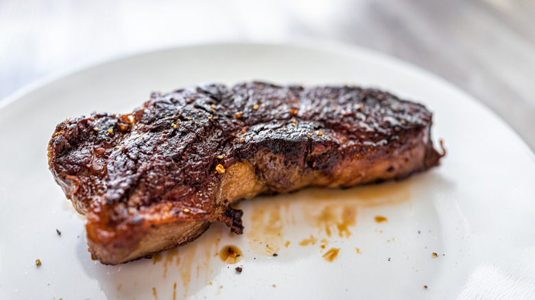 A steak with a dark crust sits on a white plate