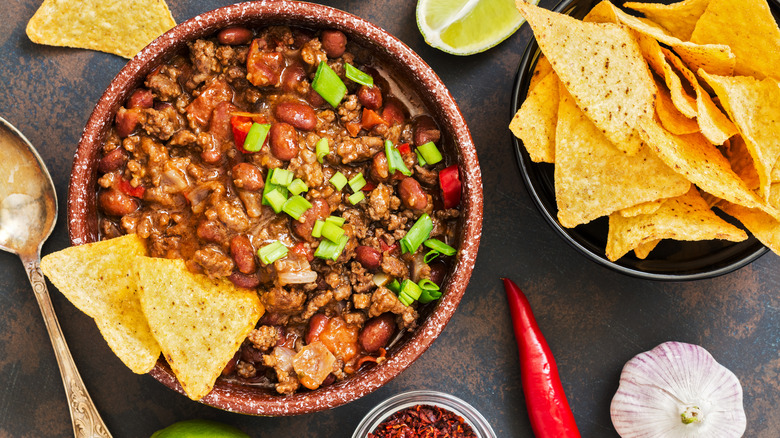 a bowl of chili topped with green onion and corn chips