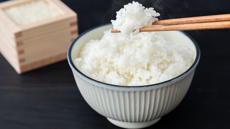 Bowl of cooked rice with chopsticks holding up rice