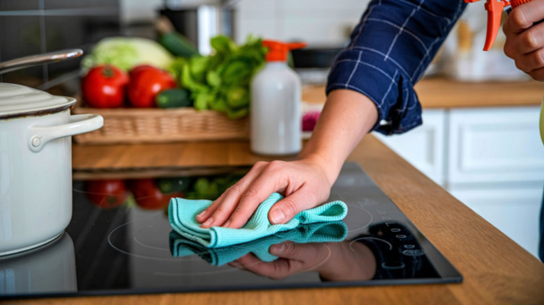 Closeup of a hand wiping an induction cooktop with a blue cloth