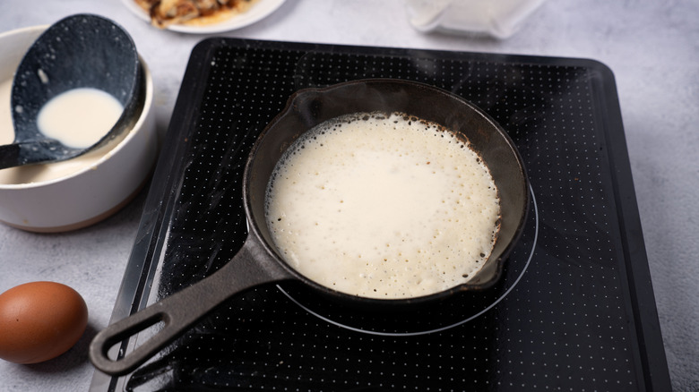 A cast-iron skillet cooks a pancake on an induction hob